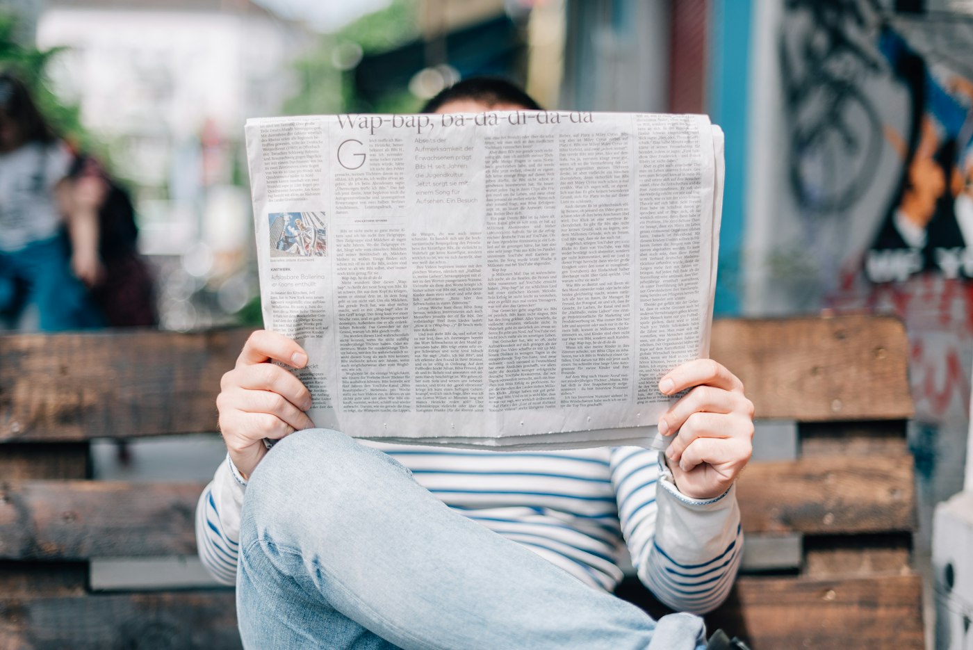 A person reading a large newspaper on a bench